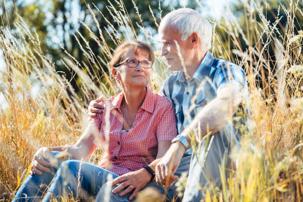 Couple of senior woman and man sitting in a meadow in the grass looking at each other